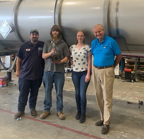 Four people standing with a trophy in workshop.