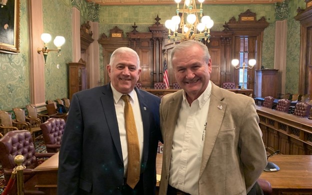 Two men smiling in elegant wood-paneled room.