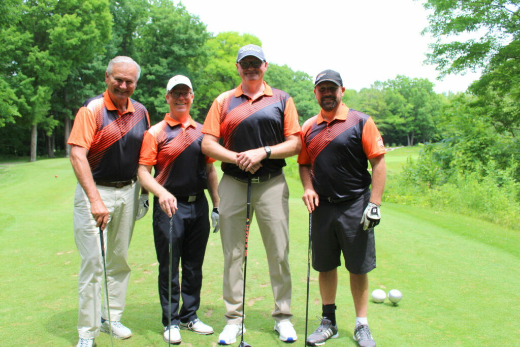 Four men in golf attire on course.