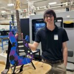 Person holding puzzle-patterned electric guitar in workshop.