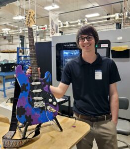 Person holding puzzle-patterned electric guitar in workshop.