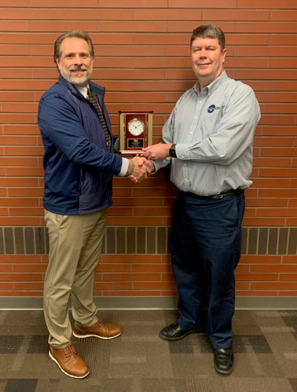 Two men shaking hands, holding clock award.