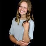 Smiling person in a gray blouse with necklace.