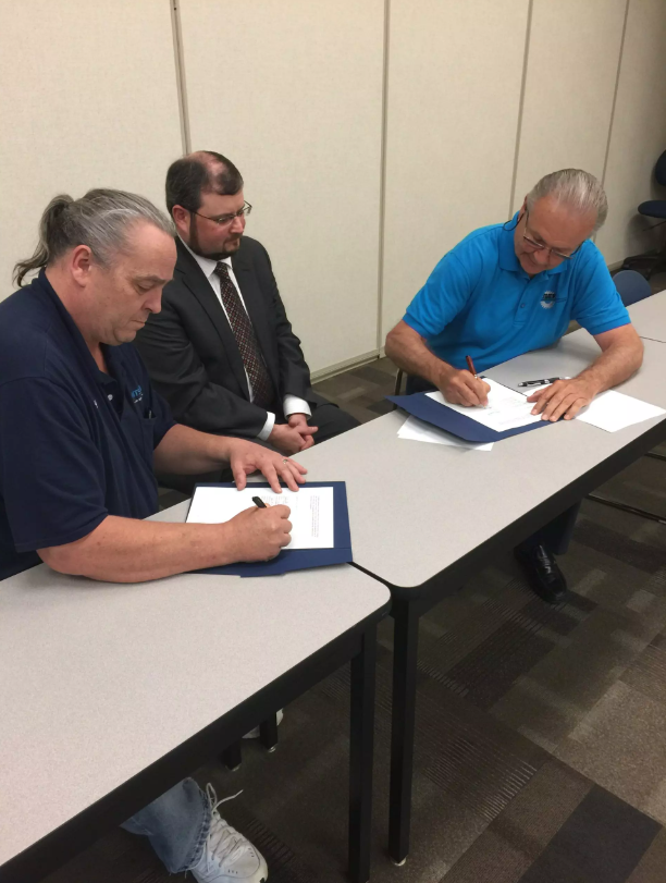 Three men signing documents at a table.