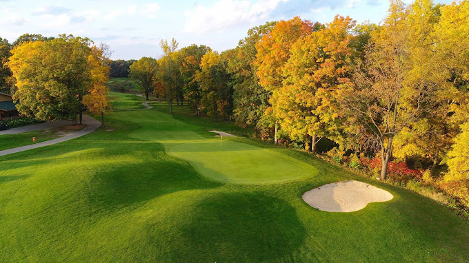 Autumn golf course with vibrant trees and sand trap.