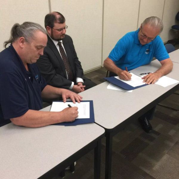 Three men signing documents at a table.