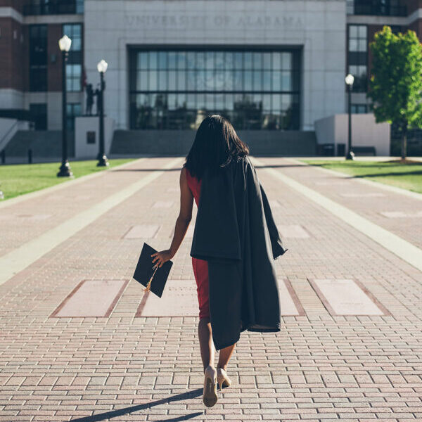 Graduate walking towards university building with cap.